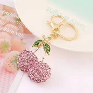 Primer plano del llavero de cereza con pedrería rosa y hojas de esmalte verde.