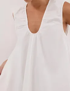 Detail of white sleeveless dress showing the deep V-neck and delicate pleated texture