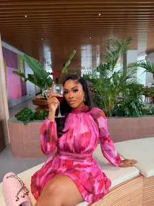 Elegant pink floral mini dress with pleated details and high neck in a chic cafe setting.