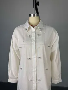 Detalle de camisa blanca de manga larga con adornos de perlas y cristales florales