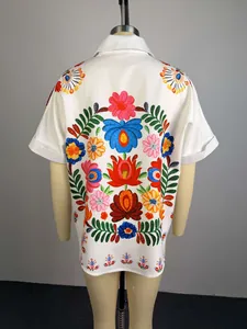 Dettaglio posteriore di camicia bianca a maniche corte con ricamo floreale colorato.