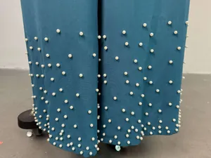 Detail of teal wide-leg pants hem featuring elegant white pearl bead embellishments