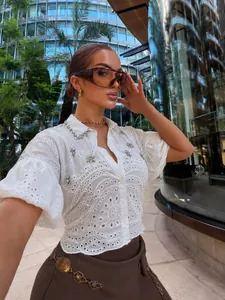 Detailed shot of white eyelet shirt with rhinestone floral accents and lantern sleeves