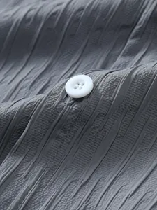 Macro view showing the gray textured striped fabric and white button of a men's shirt