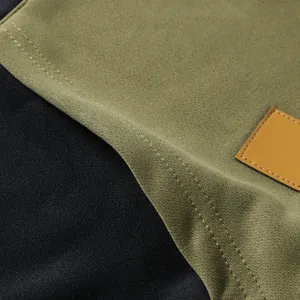 Close-up detail of color-blocked hoodie fabric showing fine stitching and leather patch.