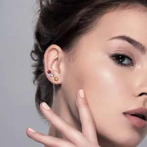 Primer plano profesional de tres pendientes de circonita de colores en la oreja de una modelo
