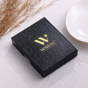 Primer plano de una caja de joyería negra texturizada con un elegante logo dorado.