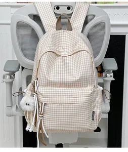 Modischer cremefarbener Karo-Rucksack für Schüler mit süßem Plüsch-Anhänger auf einem Bürostuhl.