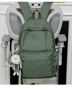 Detailansicht eines grün karierten Schulrucksacks mit einem süßen weißen Plüschanhänger.