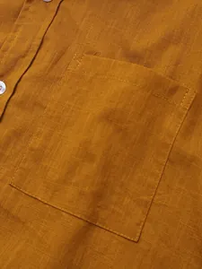 Vista detallada de la textura de la tela y el bolsillo de una camisa de lino amarillo mostaza