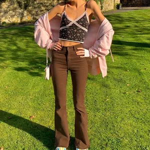Stylish woman in high-waisted brown flared denim jeans and pink hoodie standing on grass