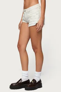 Dettaglio laterale di shorts in denim bianco a vita bassa con strappi e frange.