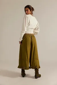 Back view of a woman wearing olive green wide-leg cropped jeans with delicate ruffle hem details