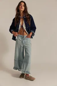 Full-length detail of light blue wide-leg cropped jeans with feminine ruffled hemline.
