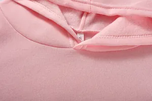 Dettaglio di una felpa rosa con cappuccio, etichetta taglia S e fodera in pile.
