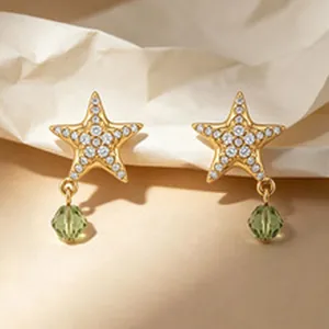 Primo piano di raffinati orecchini a stella dorati con cristalli e perla verde.