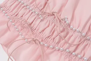 Dettaglio del tessuto plissettato rosa con delicate catene di perle e laccetti.