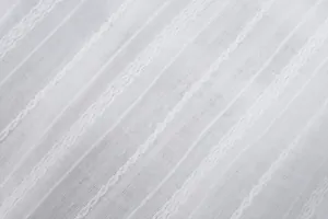 Macro view of the sheer white fabric texture with delicate vertical embroidered stripes.