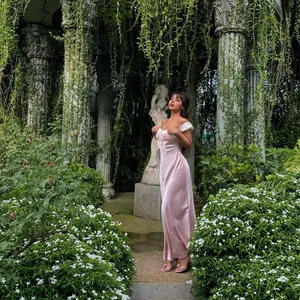 Élégante robe longue en satin rose clair de style français portée dans un jardin verdoyant luxuriant