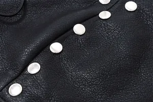 Detailed macro view of black faux leather vest with polished silver metallic studs decoration