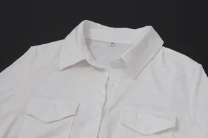Close-up detail of white collared shirt with dual chest pockets and buttons