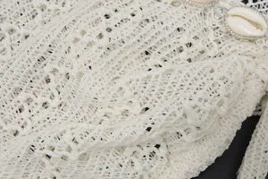 Detailed view of white crochet knit fabric featuring decorative cowrie shells and beads