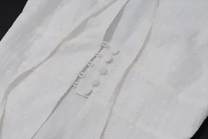 Detailed close-up of white embroidered sleeveless vest top with elegant button details