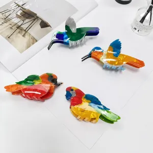 Detailansicht bunter Haarspangen in Vogelform aus Acetat auf einem offenen Magazin präsentiert.
