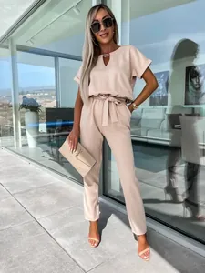 Vista completa di una tuta beige con scollo a V, cintura e dettagli metallici chic
