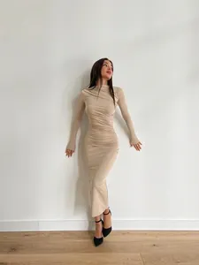 Robe longue beige moulante à manches longues présentée sur mannequin dans un décor minimaliste