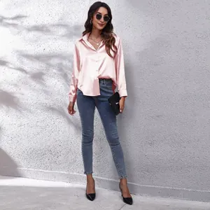Eine stilvolle Frau in einem rosa Satinhemd mit langen Ärmeln und blauen Skinny Jeans