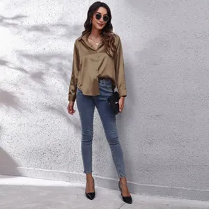 Detailansicht einer khakifarbenen Satinbluse mit langen Ärmeln und einer Jeans.