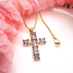 Detail of a gold cross pendant necklace featuring purple and clear square zircons.