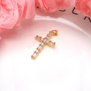 Close-up of a gold-plated cross pendant with pink marquise zircons on a white plate