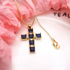 Close-up of gold-plated cross pendant featuring blue and clear cubic zirconia stones