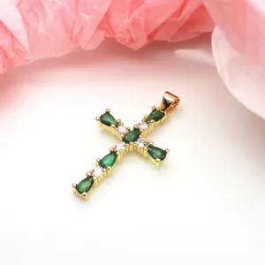 Detailed macro close-up of gold-plated cross pendant with green teardrop zircons