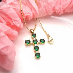 Close-up of gold cross pendant necklace featuring vibrant green round cubic zirconia