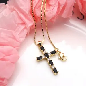 Detail shot of a gold-plated cross necklace with oval black zircons and clear crystals.