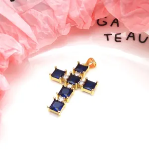 Detail of a gold-plated copper cross pendant with square blue and round white zircons.
