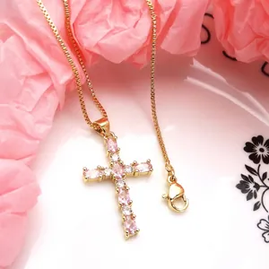 Macro detail view of a gold cross pendant necklace set with pink and clear zircon stones