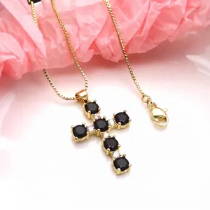 Detailed macro view of a gold cross necklace with black cubic zirconia on pink tissue paper.