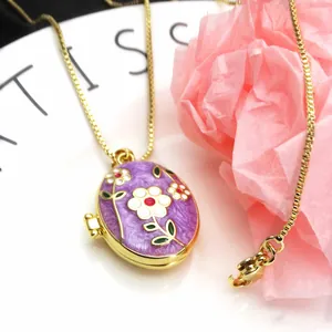 Detail view of a gold-plated oval locket necklace with purple floral enamel design.