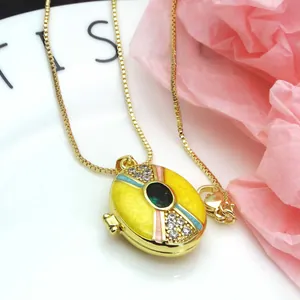 Close-up of gold plated locket necklace with yellow enamel and green stone detail