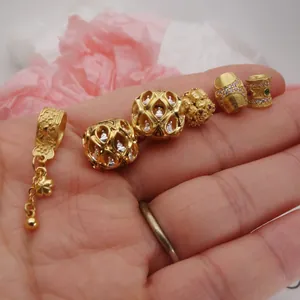 Gros plan de breloques et perles dorées pour bricolage avec des accents de zircon sur une main.
