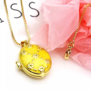 Close-up of a gold-plated oval locket necklace with yellow enamel and flower patterns