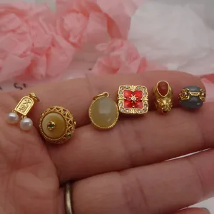 Detailed macro view of various gold-plated DIY jewelry charms and beads held in a hand