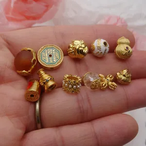 Primer plano de varias cuentas y dijes dorados para joyería DIY presentados en una mano