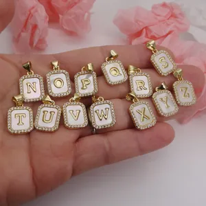 Detail view of assorted gold-plated alphabet pendants with shell inlay held in hand