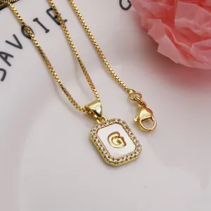 Close-up of gold square pendant with crystal borders and a shell inlay letter G design.