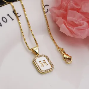Close-up of gold square letter H pendant necklace with shell and pavé zircon inlay